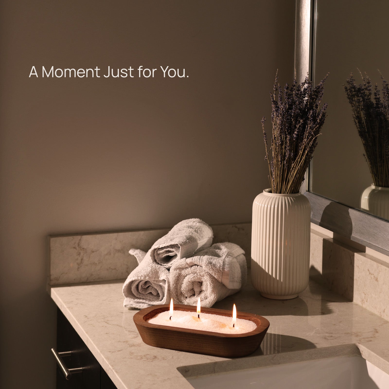 Tula white sand candle glowing on a marble bathroom counter beside lavender and soft towels — perfect for spa-like self-care rituals, intentional living, and peaceful moments at home
