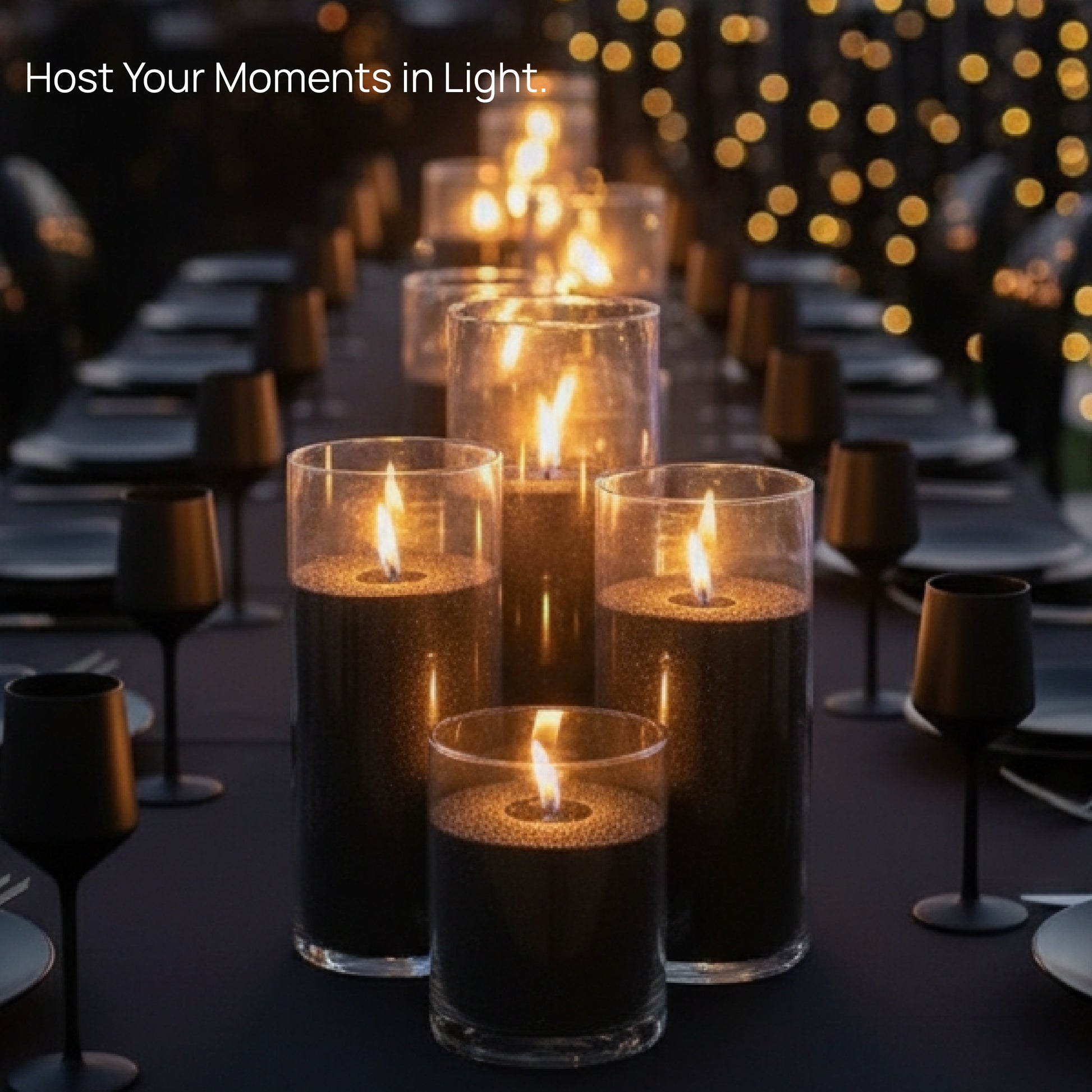 A long dinner table beautifully decorated with glowing Tula Pearled Candle Sand candles in glass containers, surrounded by matte black tableware and warm string lights in the background, creating an elegant evening ambiance.