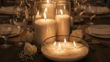 Wedding table set with Tula candle sand burning in glass vases among white roses and wine glasses.