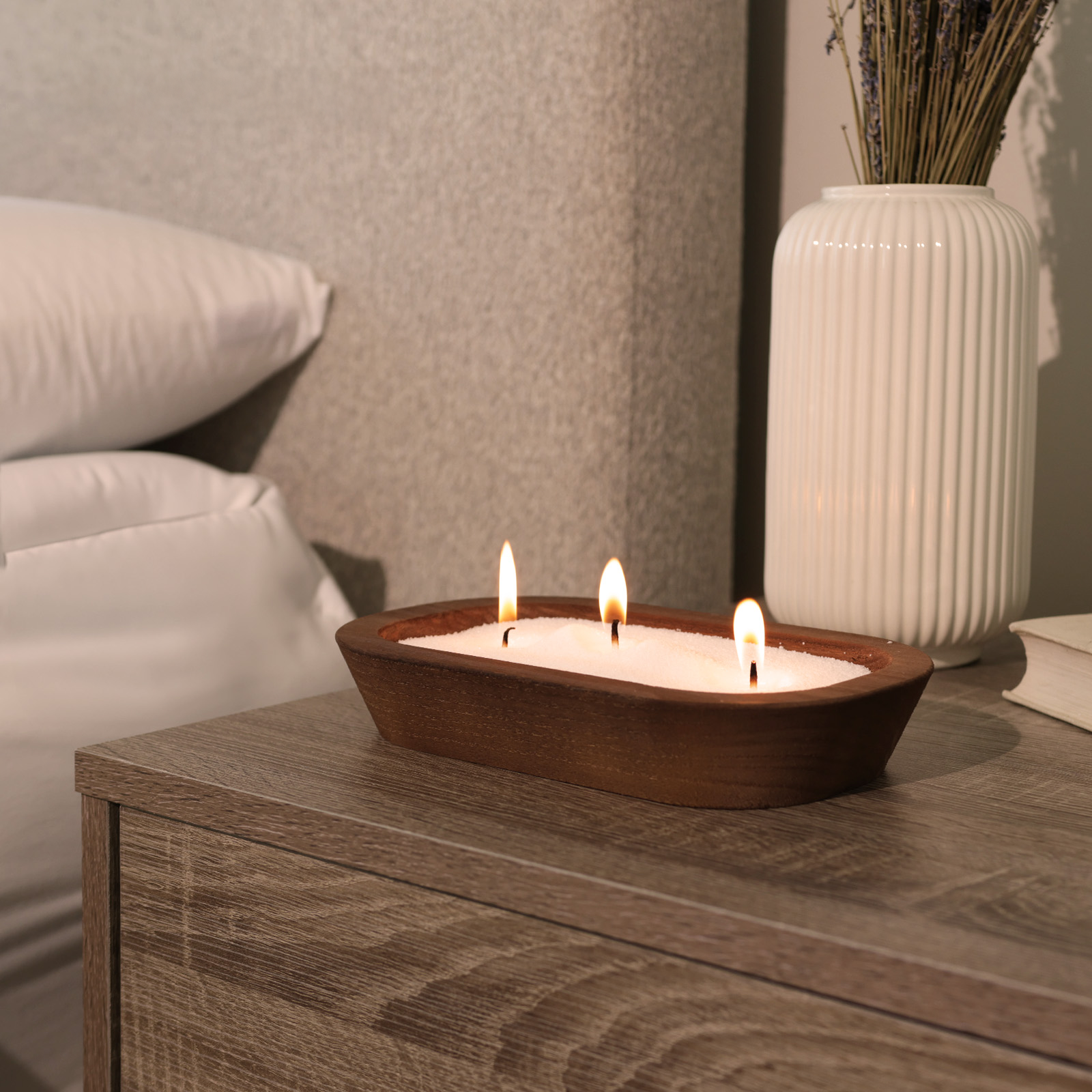 Tula white sand candle burning in a handcrafted wooden bowl on a nightstand, beside soft pillows and a ceramic vase — ideal for bedtime rituals, minimalist decor, and calm, intentional living.
